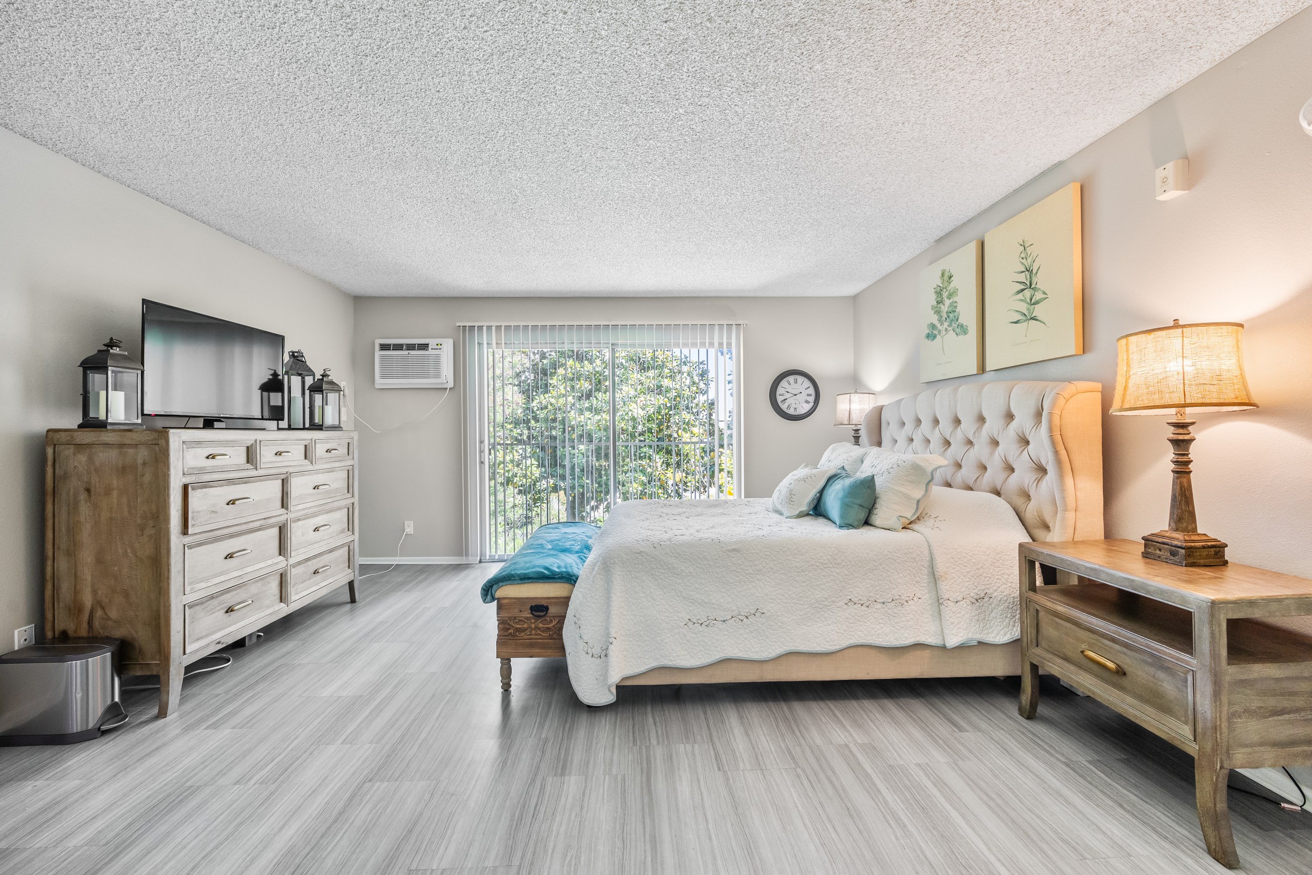 A bedroom with a large bed, a wooden dresser, and a window with blinds.